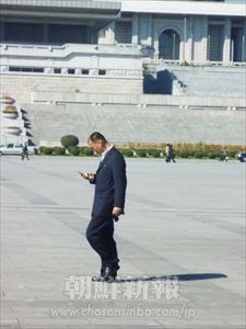 金日成広場を歩く男性。よく見ると携帯電話が…。