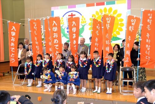 「入学おめでとう応援隊」の参加者たちは、オレンジののぼりを掲げ新入生たちを祝った